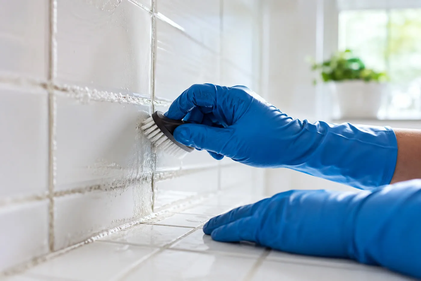 Hands scrubbing tile grout in a bright bathroom during a deep clean